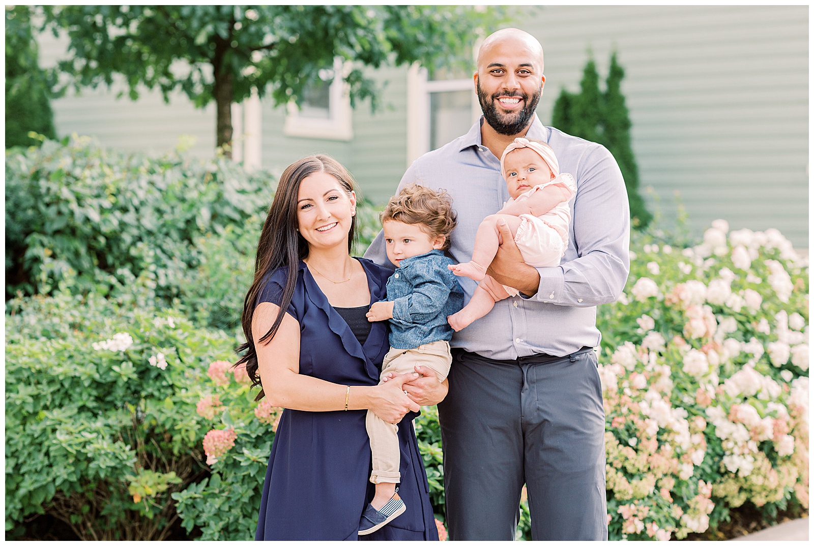 Parents smiling into camera while holding young son and baby daughter newmarket family session